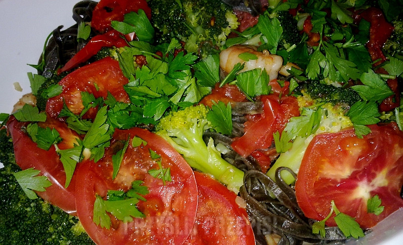 Czarny makaron podany z krewetkami, brokułami i pomidorami